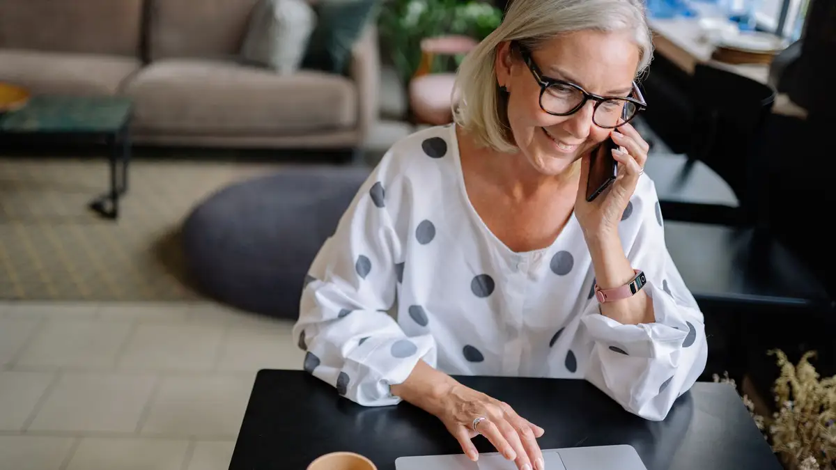Senior woman with coffee taking a phone call at home
