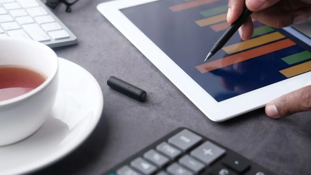 Financial charts on a tablet next to a cup of tea